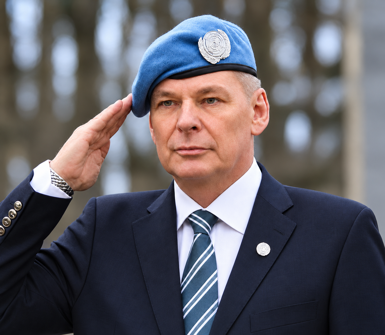 Mann i mørk dress og blå FN-beret hilser militært under en seremoni. FN-emblemet er synlig på bereten og jakkeslaget.